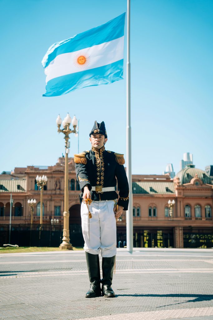 Argentinian soldier stands guard in front of the iconic Casa Rosada with national flag waving.